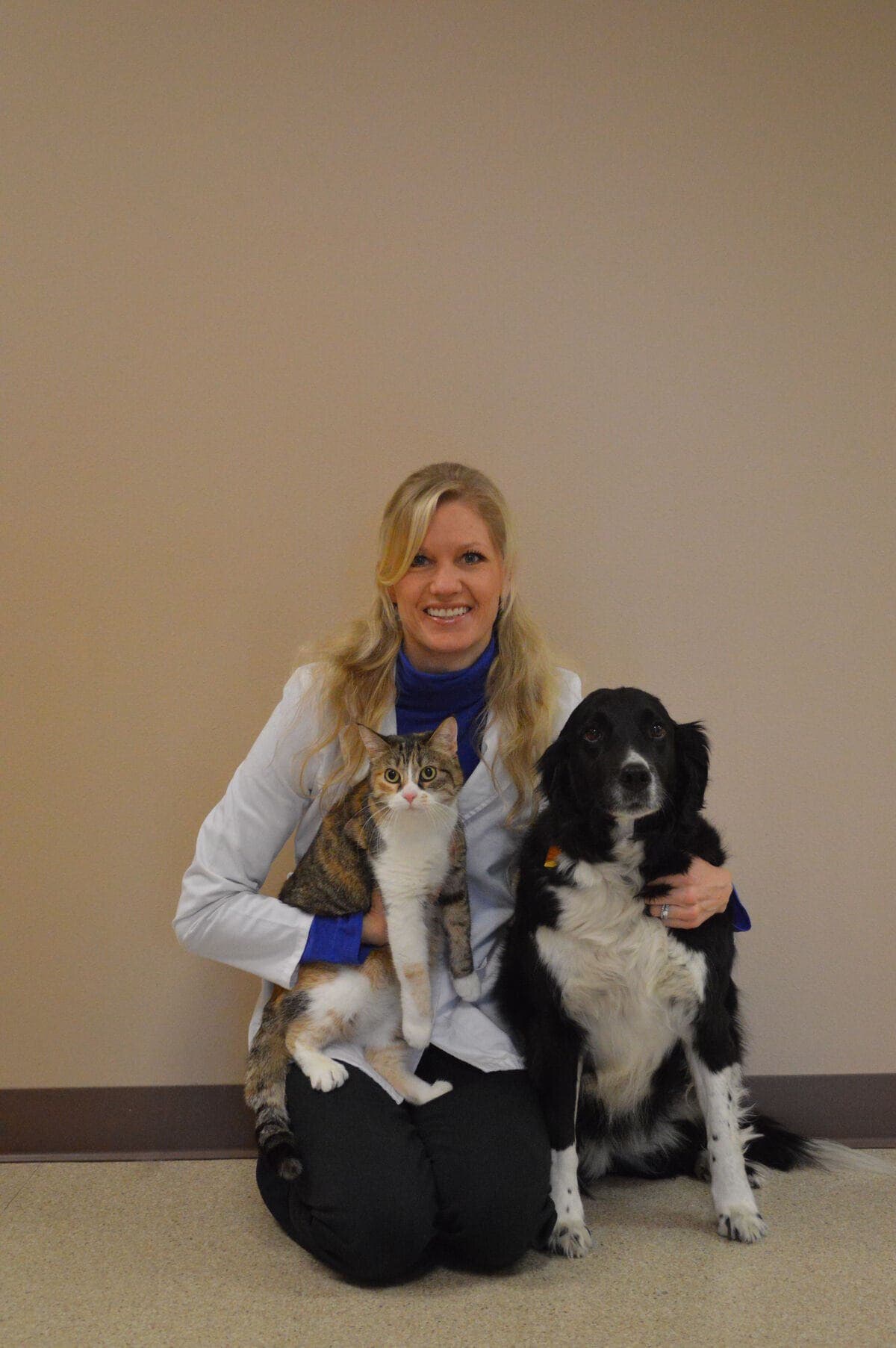 Dr. Andrea Ray kneeling in her white coat with a tabby cat and a black and white dog