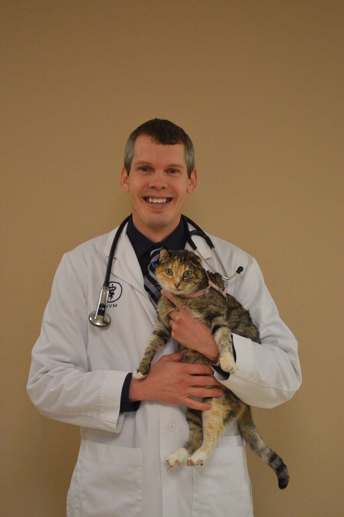 Dr. Tom Rentschler in his DVM coat, holding a calico-tabby cat