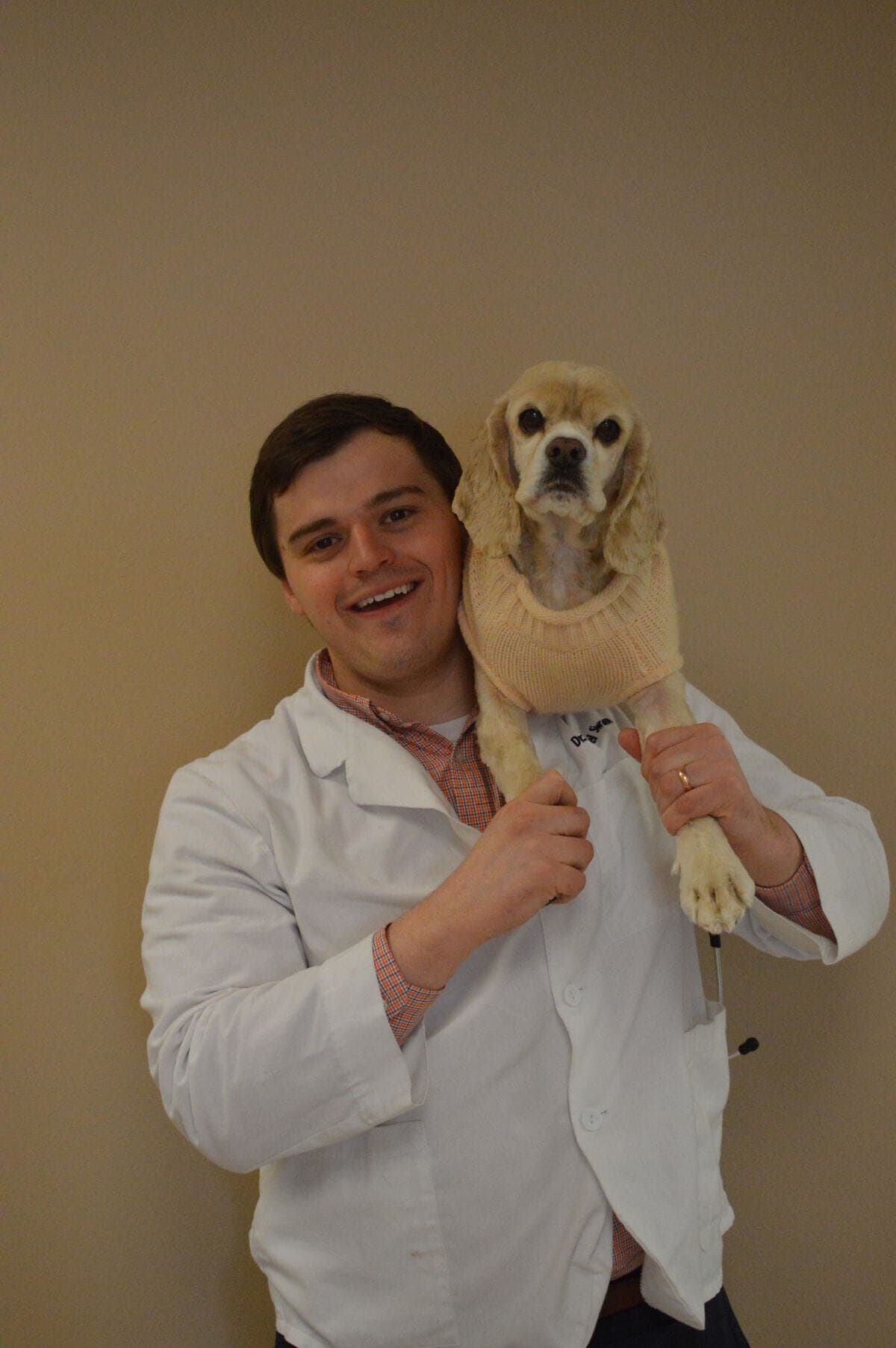 Dr. Michael Swann holding a buff cocker spaniel wearing a knit sweater